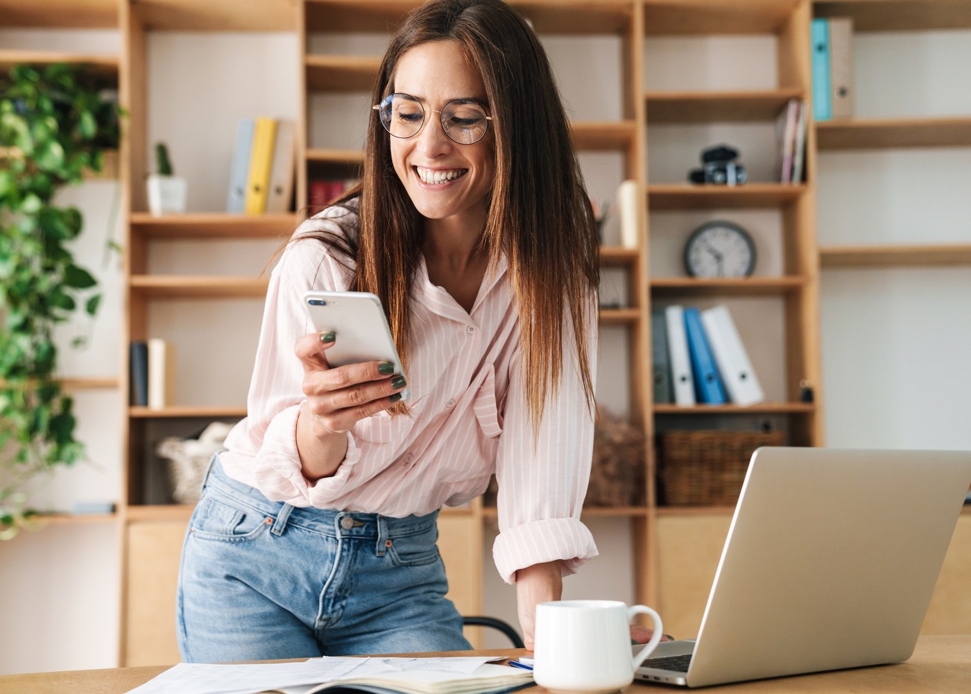 A marketer checking incoming leads on a phone beside an open laptop.